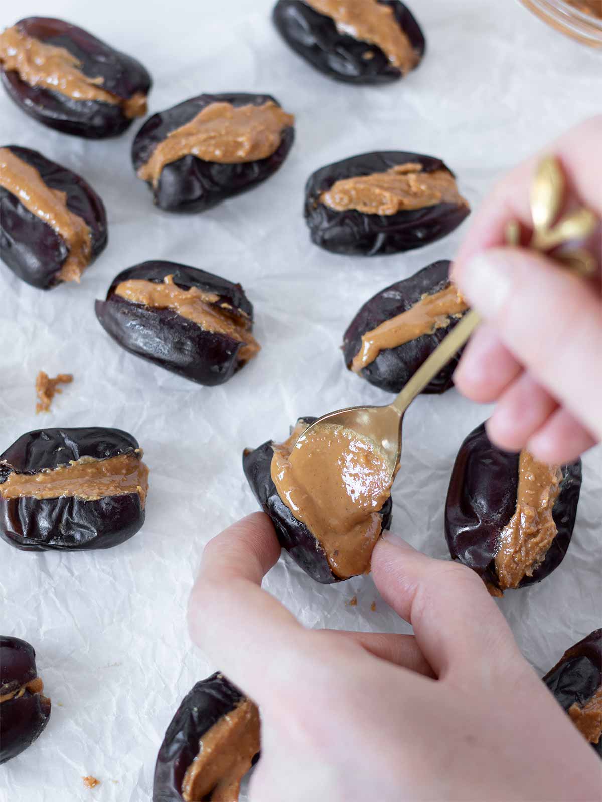 Hand filling dates with spoonful of natural creamy peanut butter