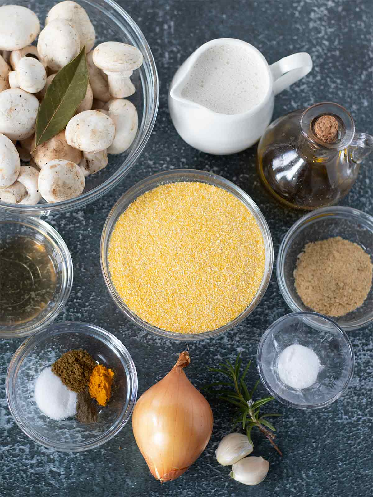Plant-based ingredients for preparing homemade savory mushroom polenta recipe: polenta, white mushrooms, dairy-free milk, olive oil, onion, garlic, nutritional yeast, white wine, salt and spices