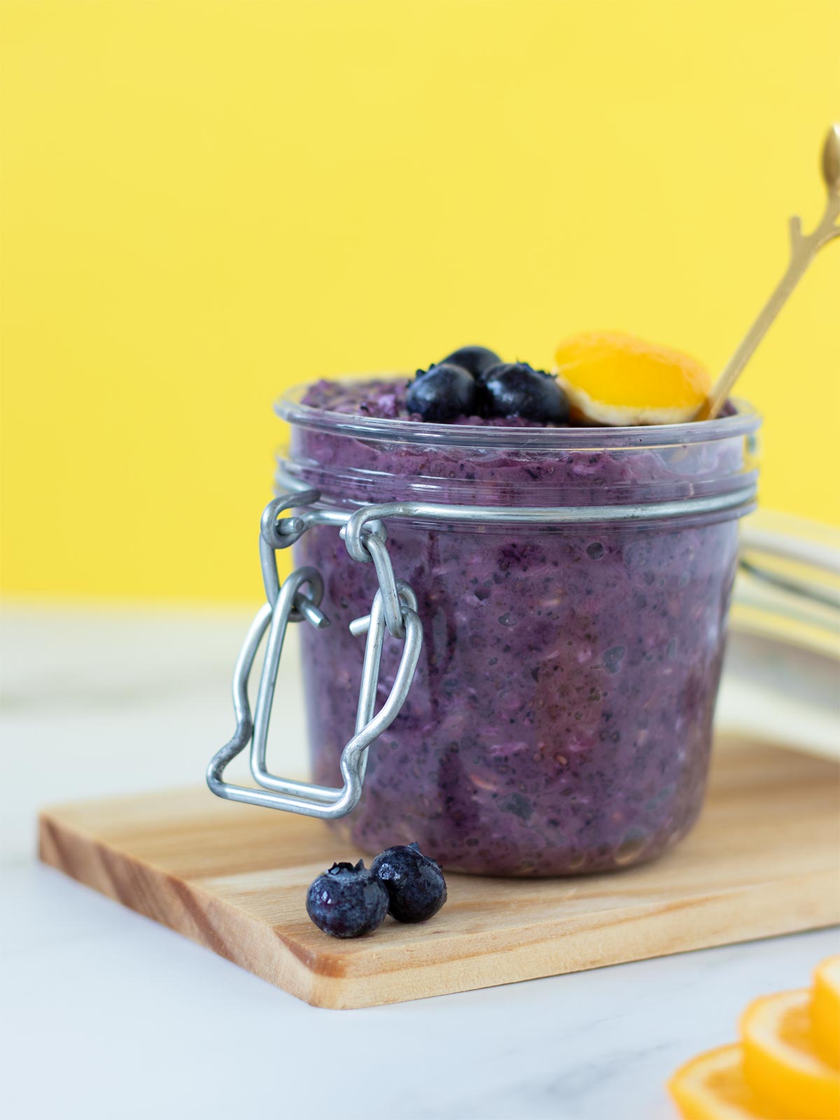 Healthy overnight oats with frozen blueberries, lemon, chia seeds, and peanut butter in a jar with yellow background
