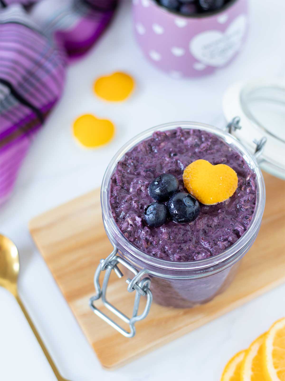 Colorful blueberry lemon overnight oats in a jar with golden spoon and lemon peel hearts