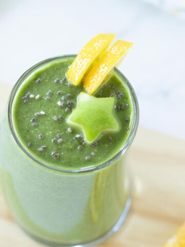 Green detox smoothie in a glass decorated with fresh lemon slices and carved apple star on a small wooden cutting board