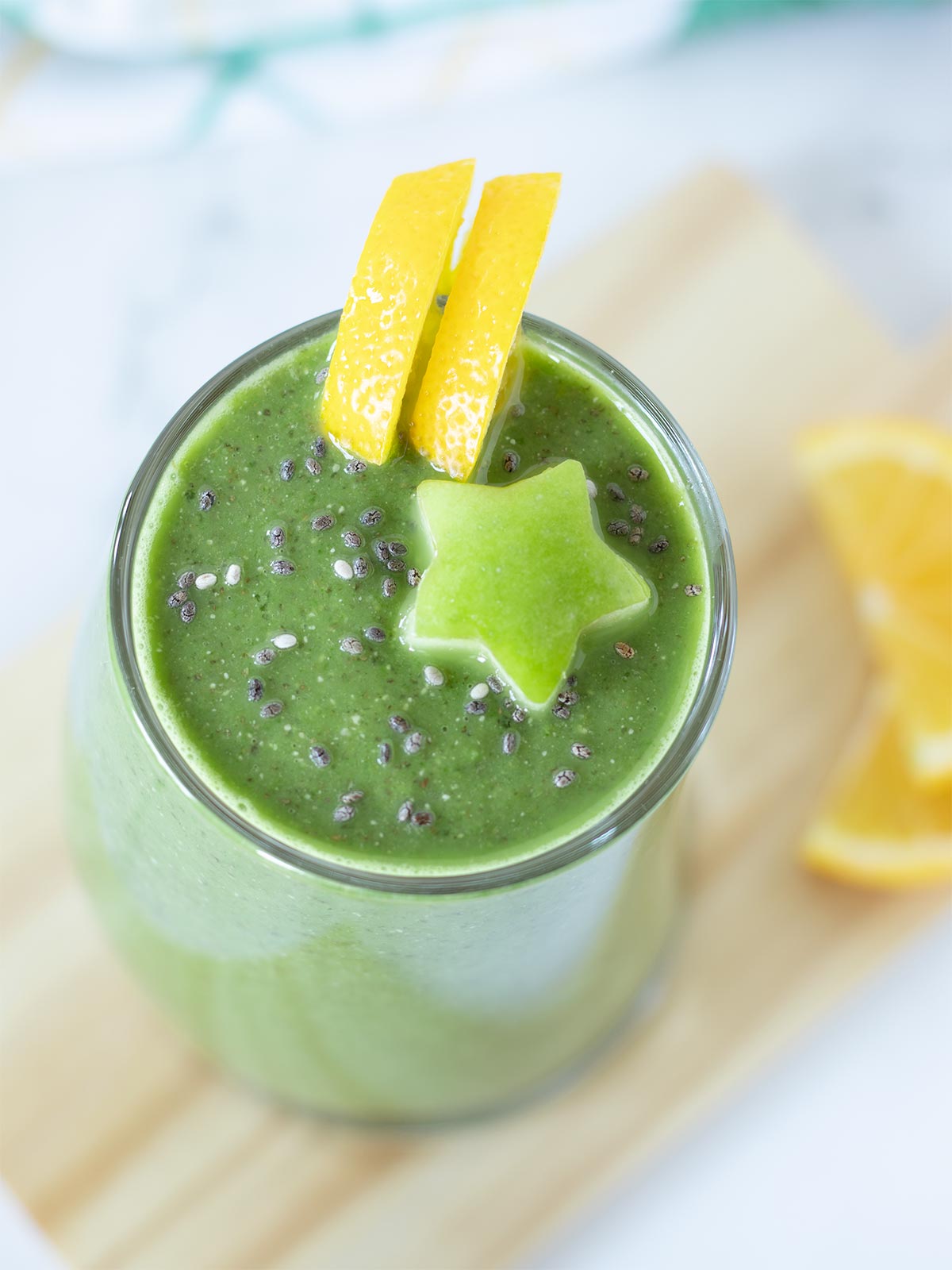 Vegan detox drink made from fresh spinach, fruits, and chia seeds in a glass garnished with carved green apple star and lemon slices.