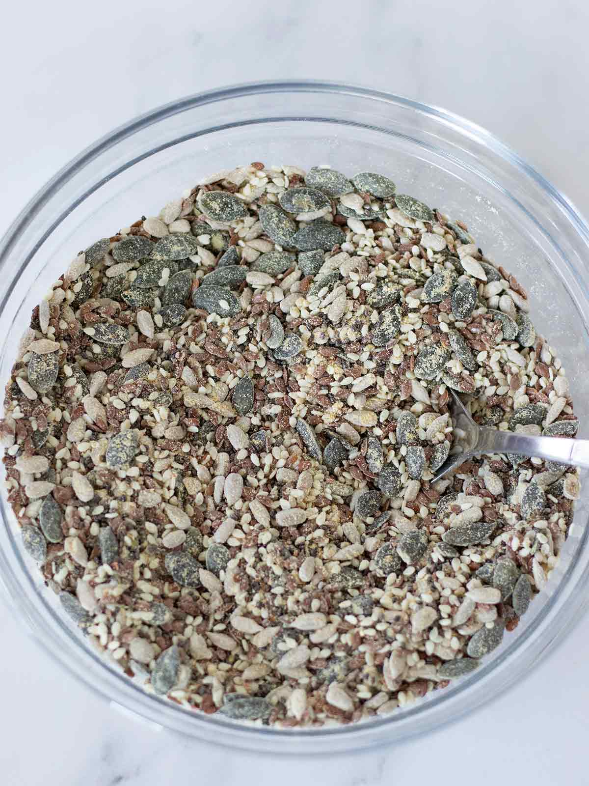 5 mixed seeds, chickpea flour, salt, herbs, and spices in glass bowl