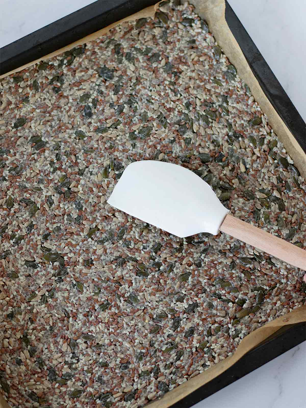 Silicon spatula over baking sheet covered with parchment paper  filled with vegan gluten-free super seed dough prepred for baking