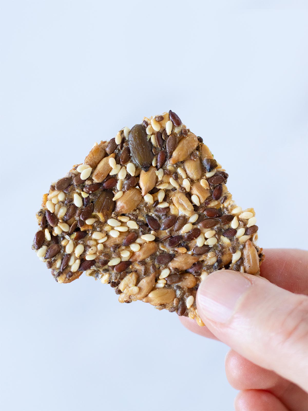 Female hand is holding a multi seed cracker (gluten-free) with white background