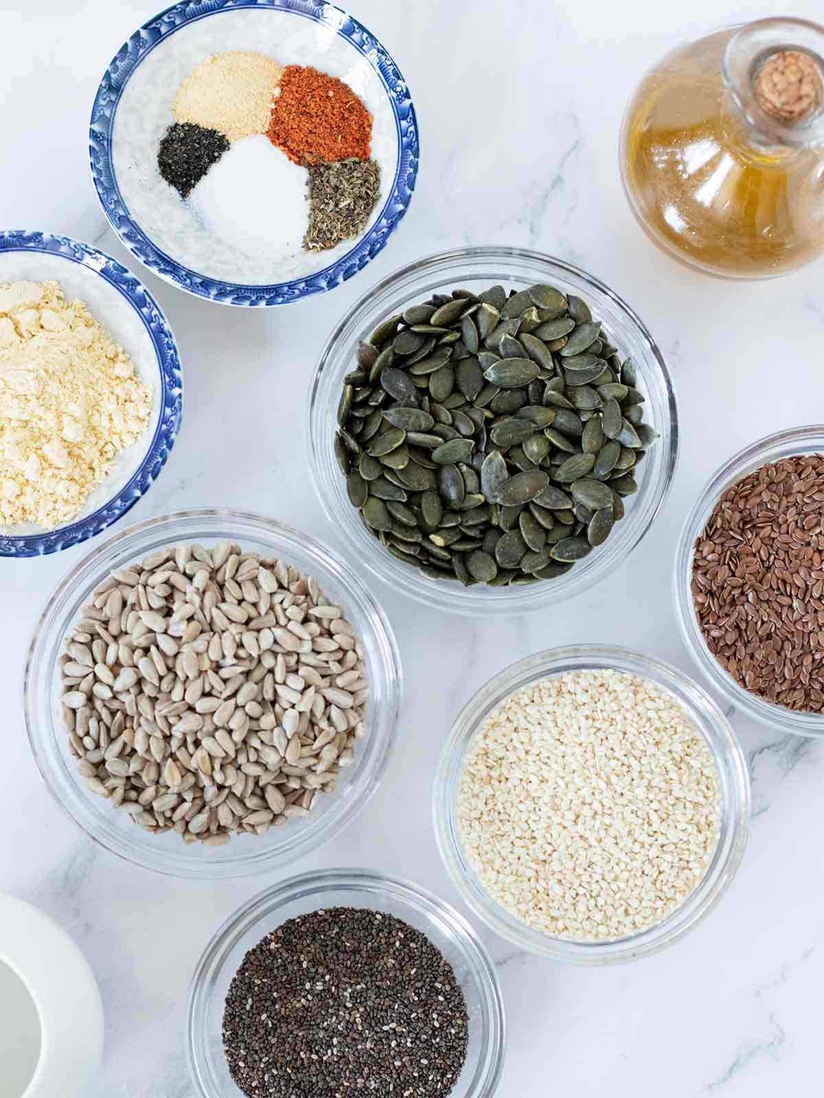 Plant-based ingredients for making homemade vegan gluten-free seed crackers: sunflower seeds, pumpkin seeds, sesame seeds, flax seeds, chia seeds, chickpea flour, olive oil, salt, herbs and spices