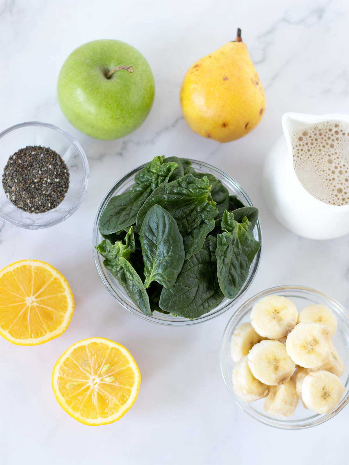 Plant-based ingredients for making homemade weight loss morning drink: spinach leaves, oat milk, green apple, pear, frozen banana, chia seeds and lemon.