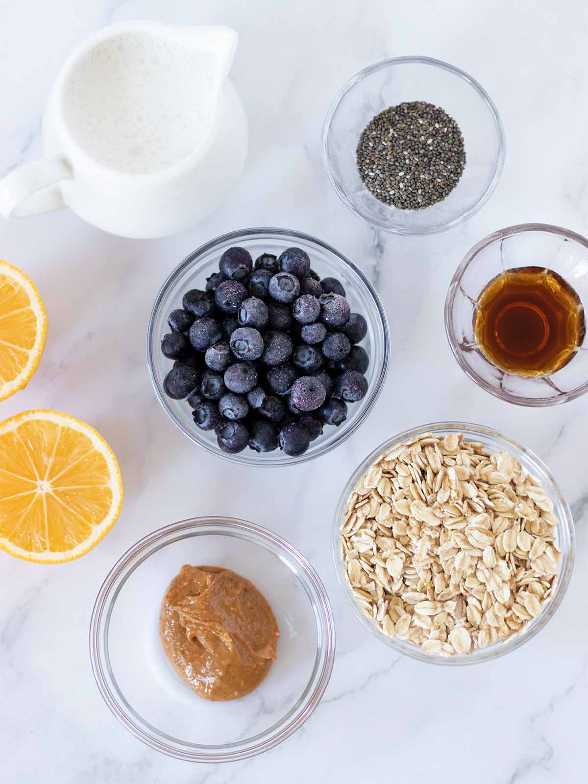 Plant-based ingredients for preparing overnight oats: frozen blueberries, oat milk, rolled oats, peanut butter, chia seeds, pure maple syrup, and lemon