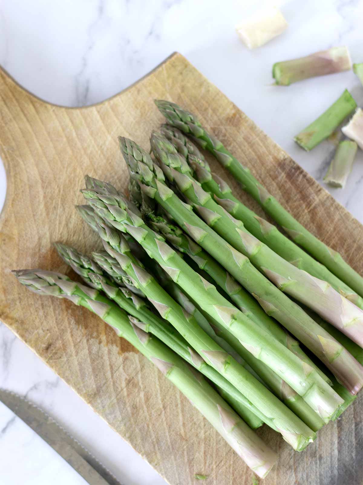 Fresh asparagus stalks on wooden cutting board with sliced bottom parts