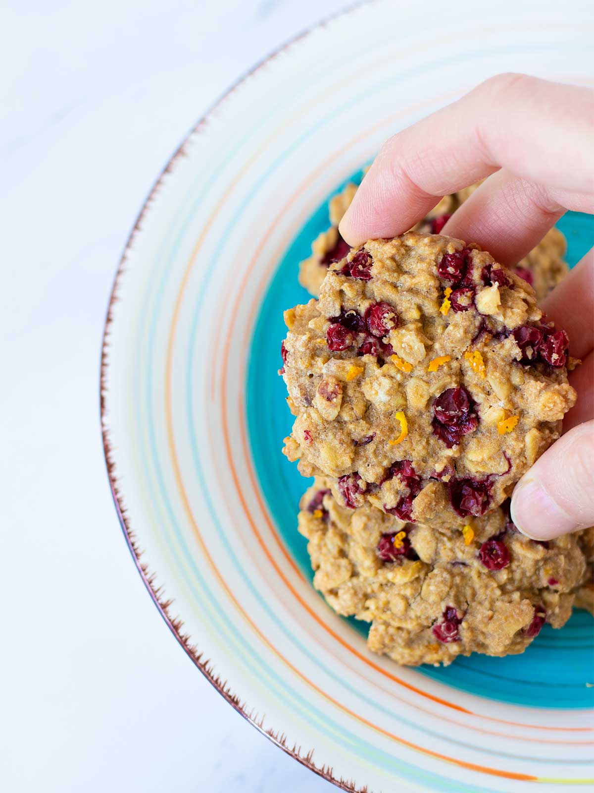 Female hand is holding chewy eggless cookie made with frozen cranberries and orange zest