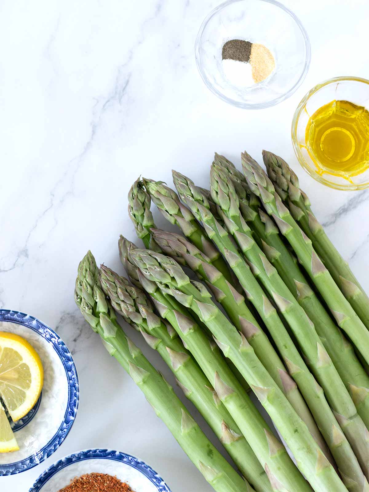 Simple ingredients for cooking oven-roasted asparagus recipe: fersh asparagus stalks, extra virgin olive oil, salt, spices, red pepper flakes and freshly squeezed lemon juice
