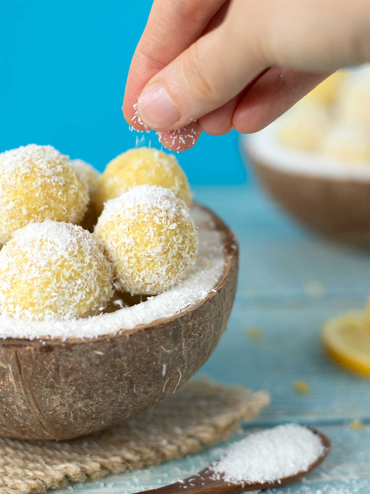 Female fingers sprinkle desiccated coconut flakes on a sugar-free energy balls placed in a coconut shell