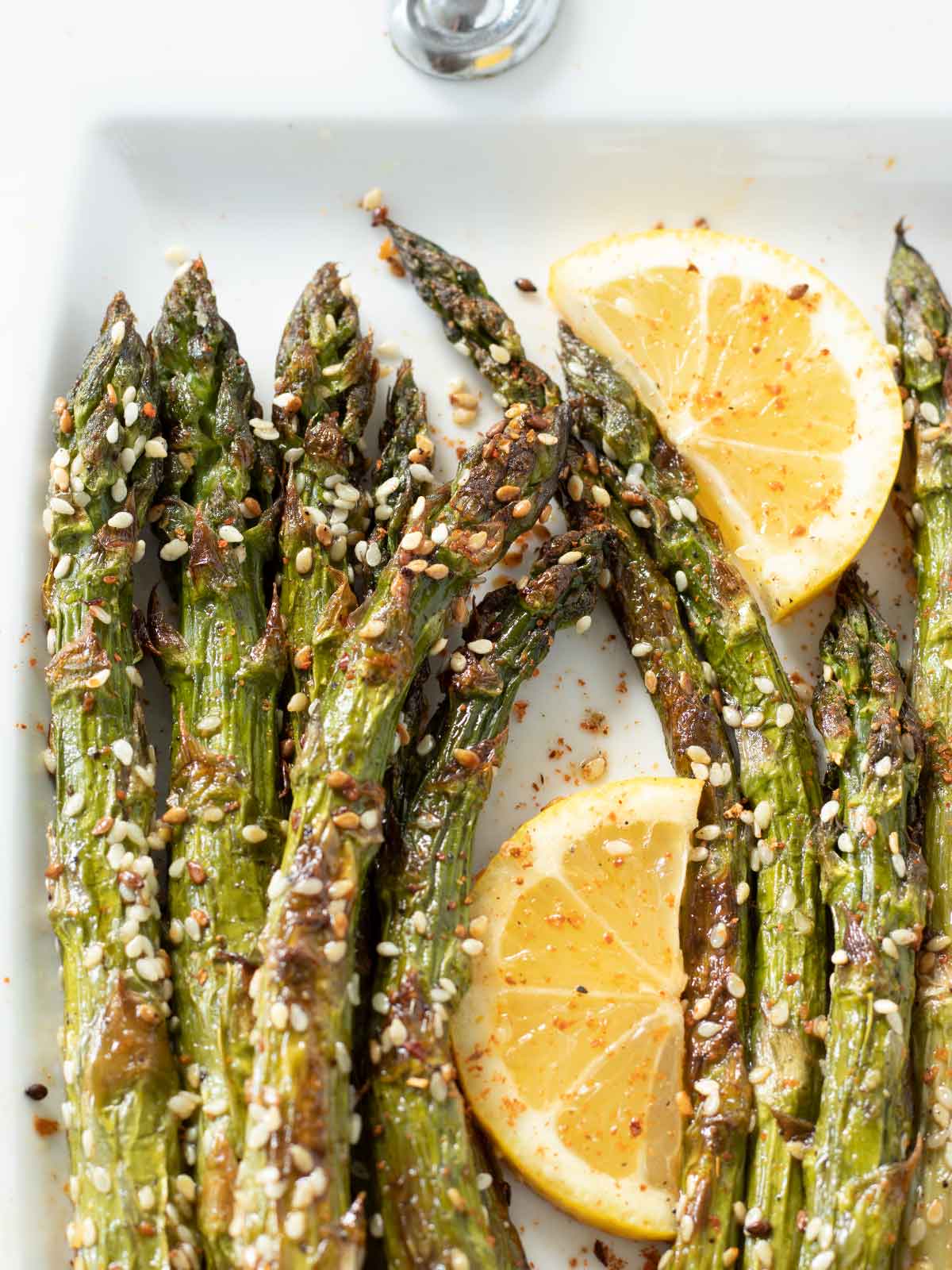 Asparagus stalks roasted in the oven with sesame seeds and sprinkled with red pepper flakes and fresh lemon slices