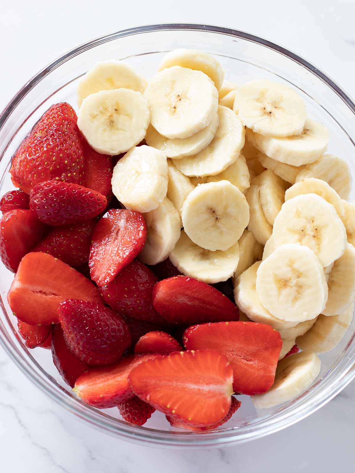 Halved fresh strawberries and sliced bananas in a salad bowl