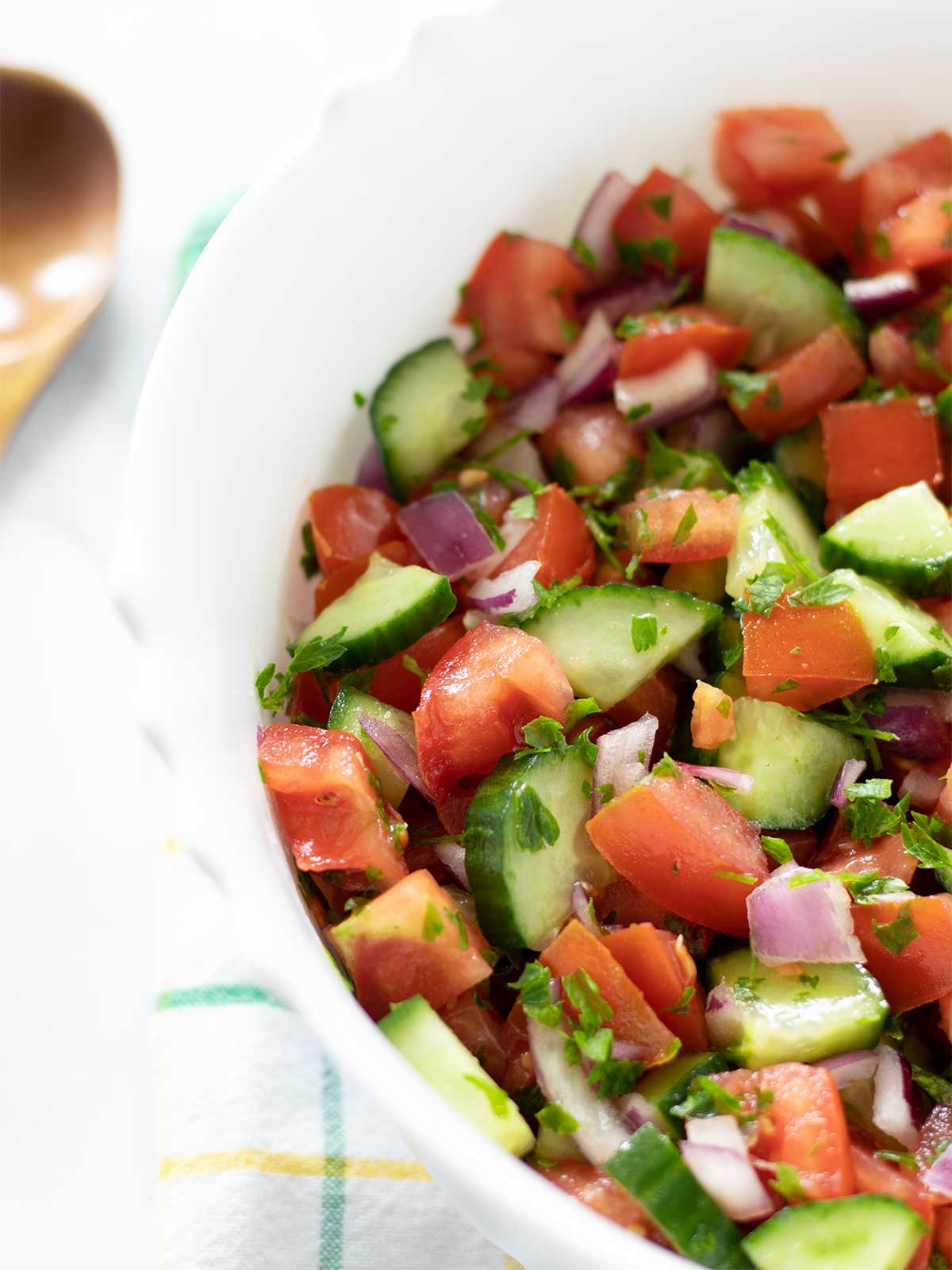Vegan cucumber tomato salad for a crowd in a big bowl with wooden spoon and kitchen towel