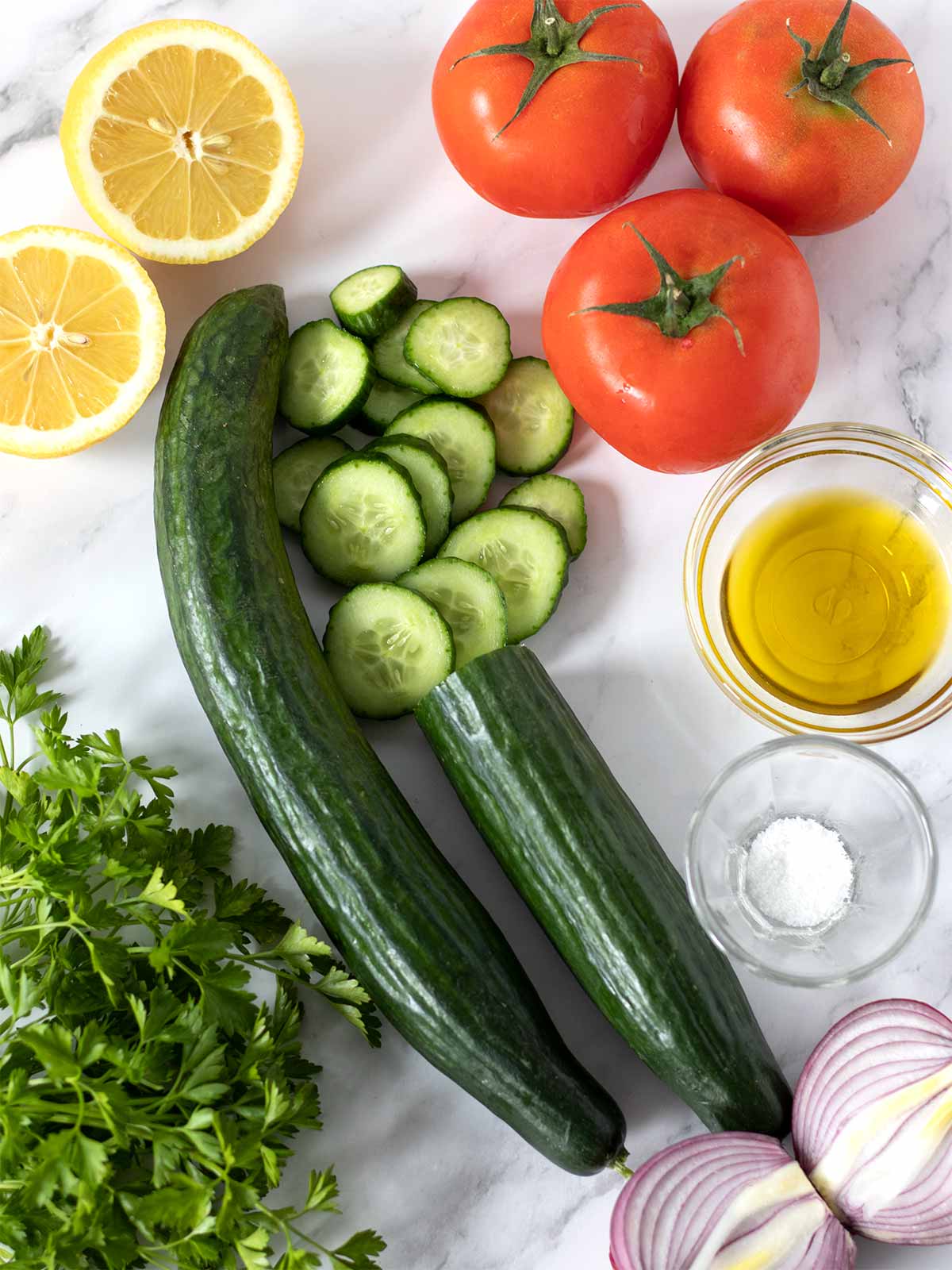 Fresh whole foods for preparing healthy low-calorie salad side dish: cucumbers, tomatoes, red onion, parsley, lemon, extra virgin olive oil, and salt.