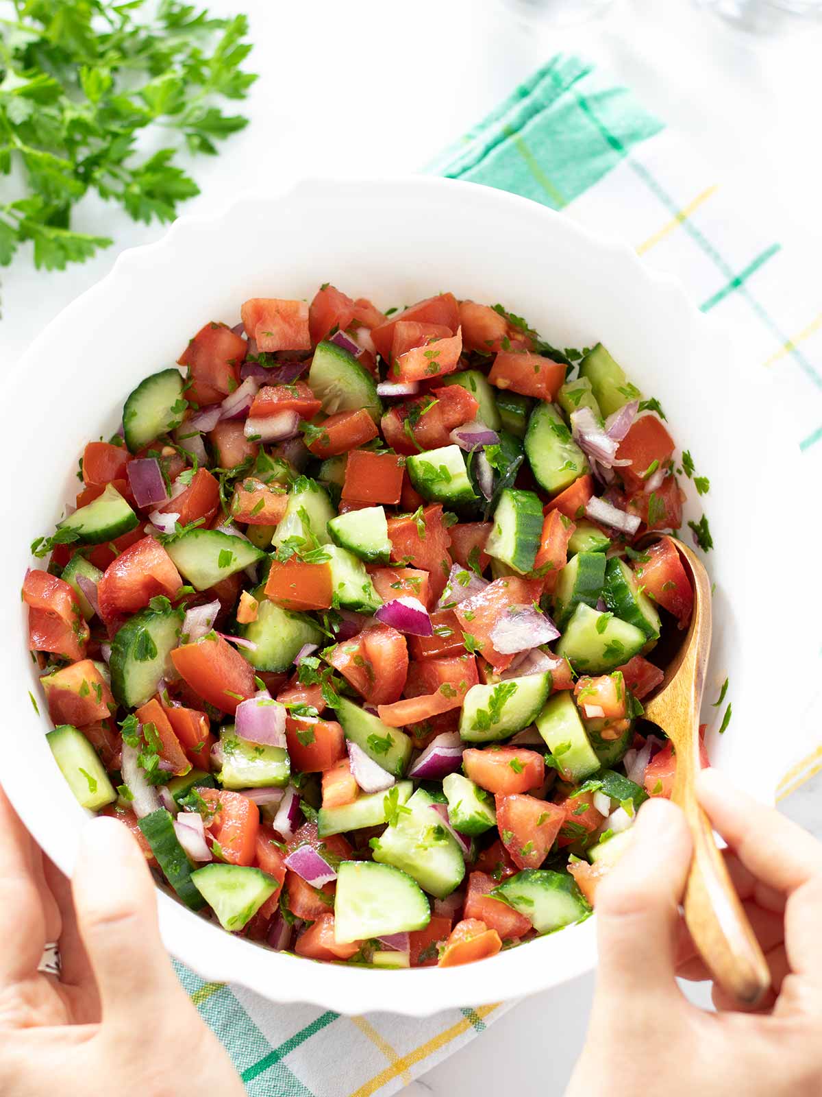 Mediterranean cucumber tomato onion salad with parsley in a bowl with female hands holding a wooden spoon