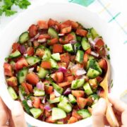 Mediterranean cucumber tomato onion salad with parsley in a bowl with female hands holding a wooden spoon