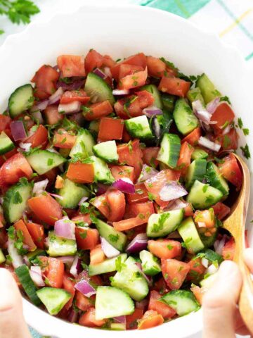 Mediterranean cucumber tomato onion salad with parsley in a bowl with female hands holding a wooden spoon