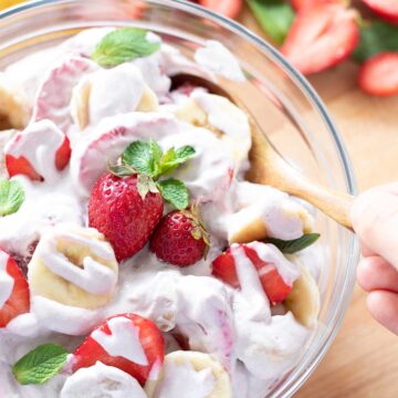 Fresh Strawberry banana cheesecake salad in a bowl with female hand holding wooden spoon
