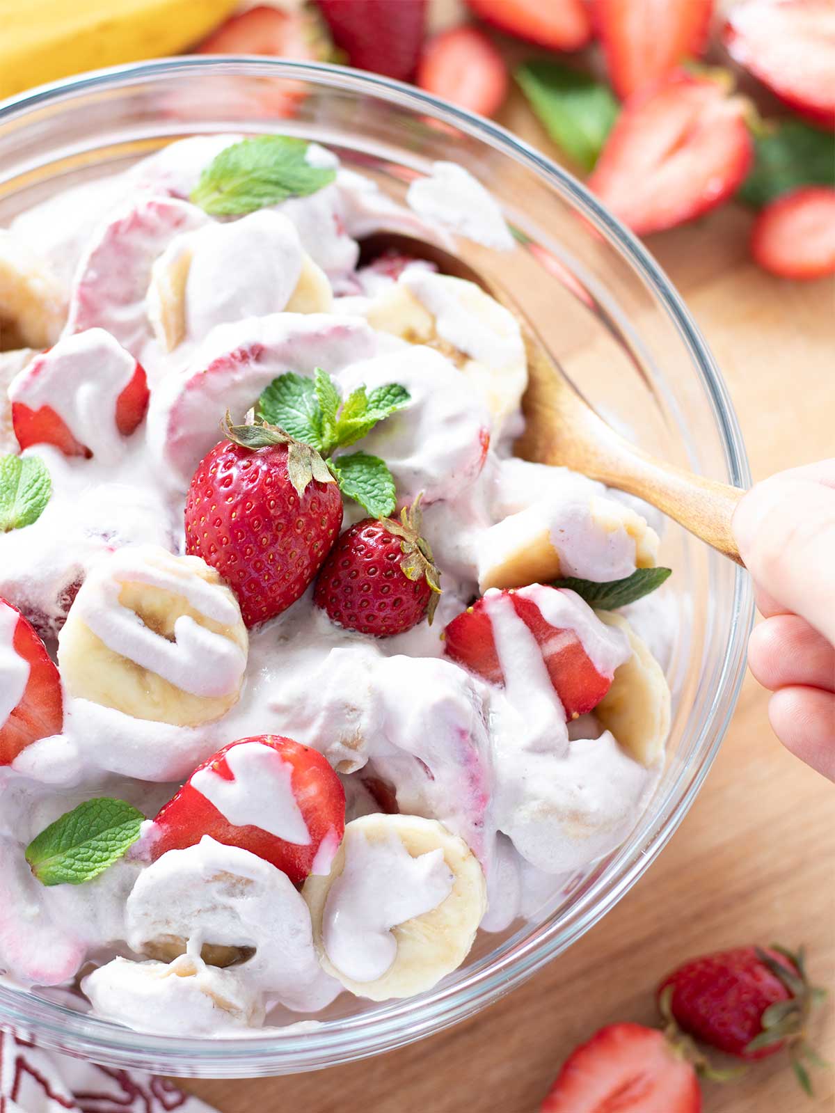 Fresh Strawberry banana cheesecake salad in a bowl with female hand holding wooden spoon