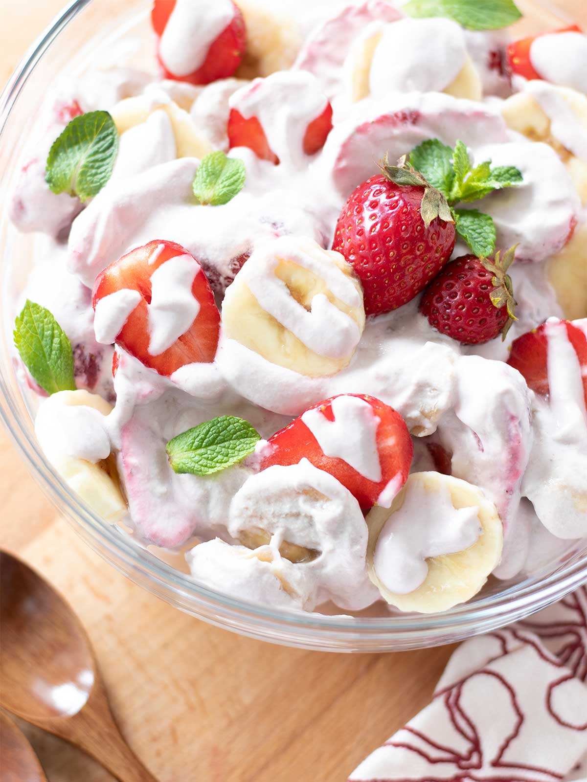 Delicious summer dessert salad with creamy cashew strawberry dressing decorated with fresh mint leaves on table with wooden spoon and kitchen towel