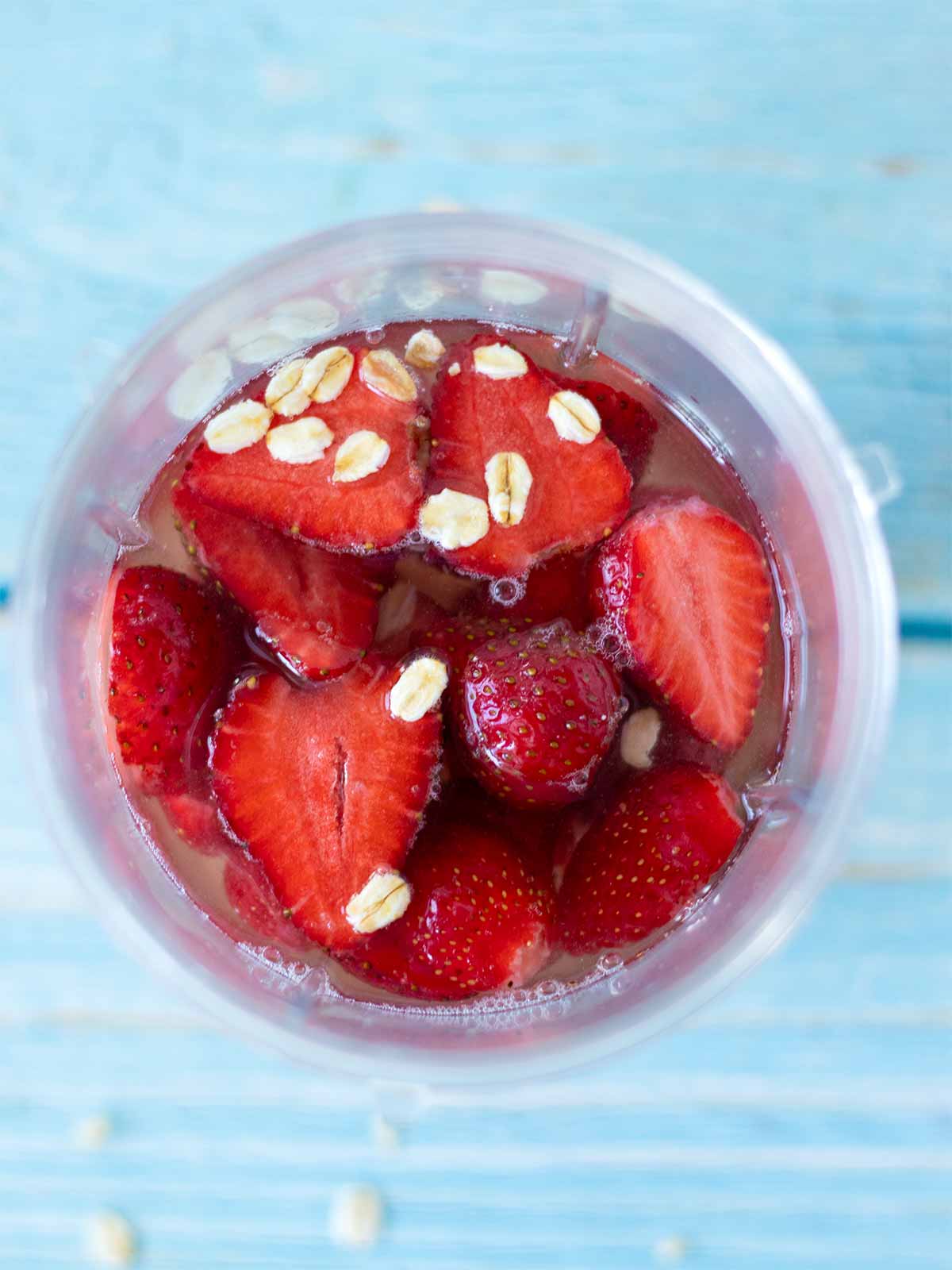 Fresh ingredients in a blender cup for preparing refreshing homemade strawberry flavored milk at home