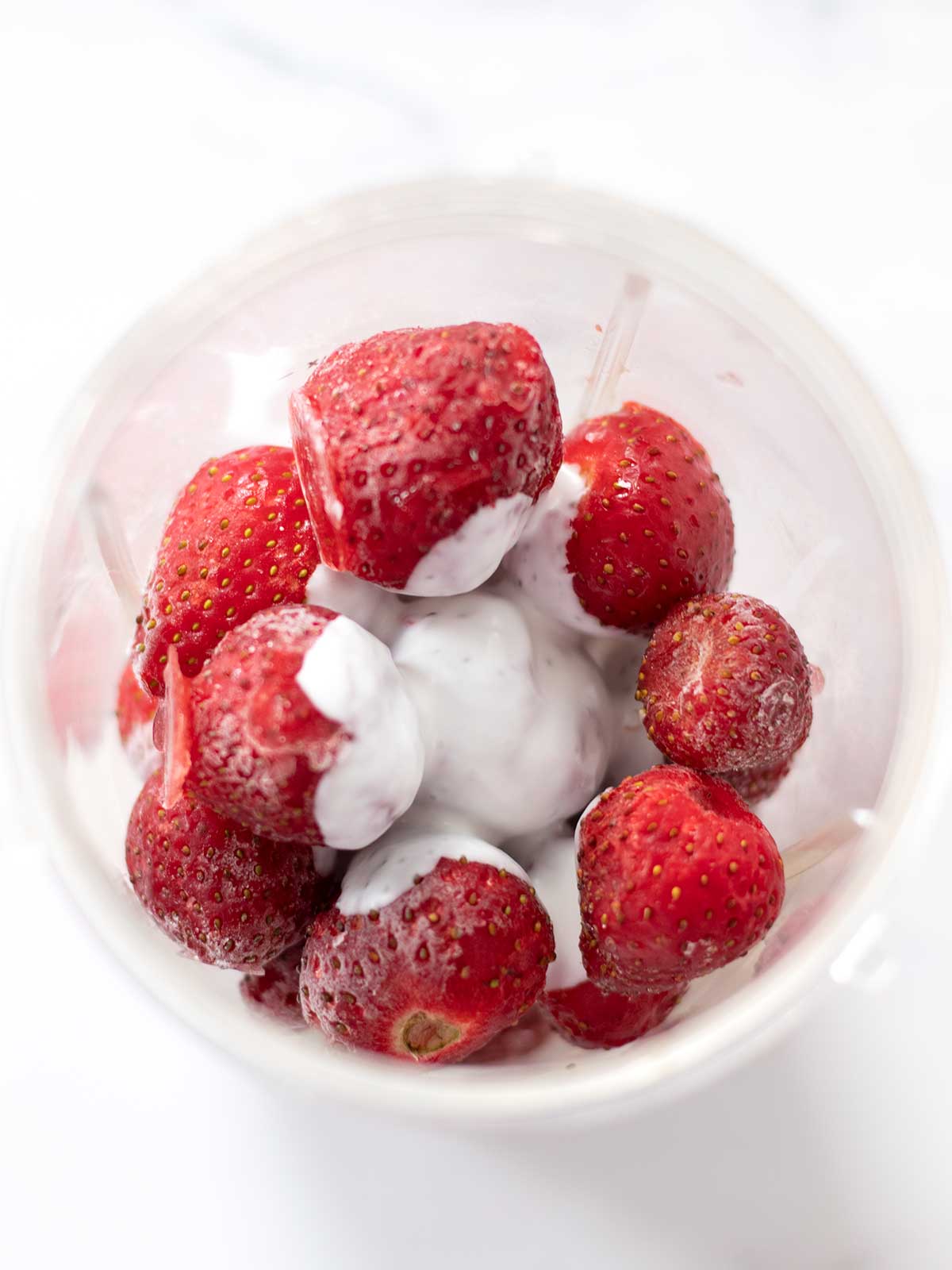 Brozen strawberries and dairy-free coconut milk in a blender cup
