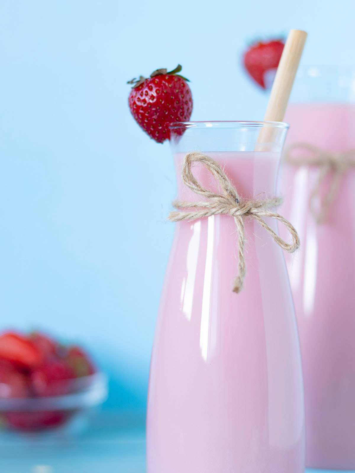 Healthy non dairy strawberry flavored milk in glass bottle with decorated with fresh strawberries and bamboo straw