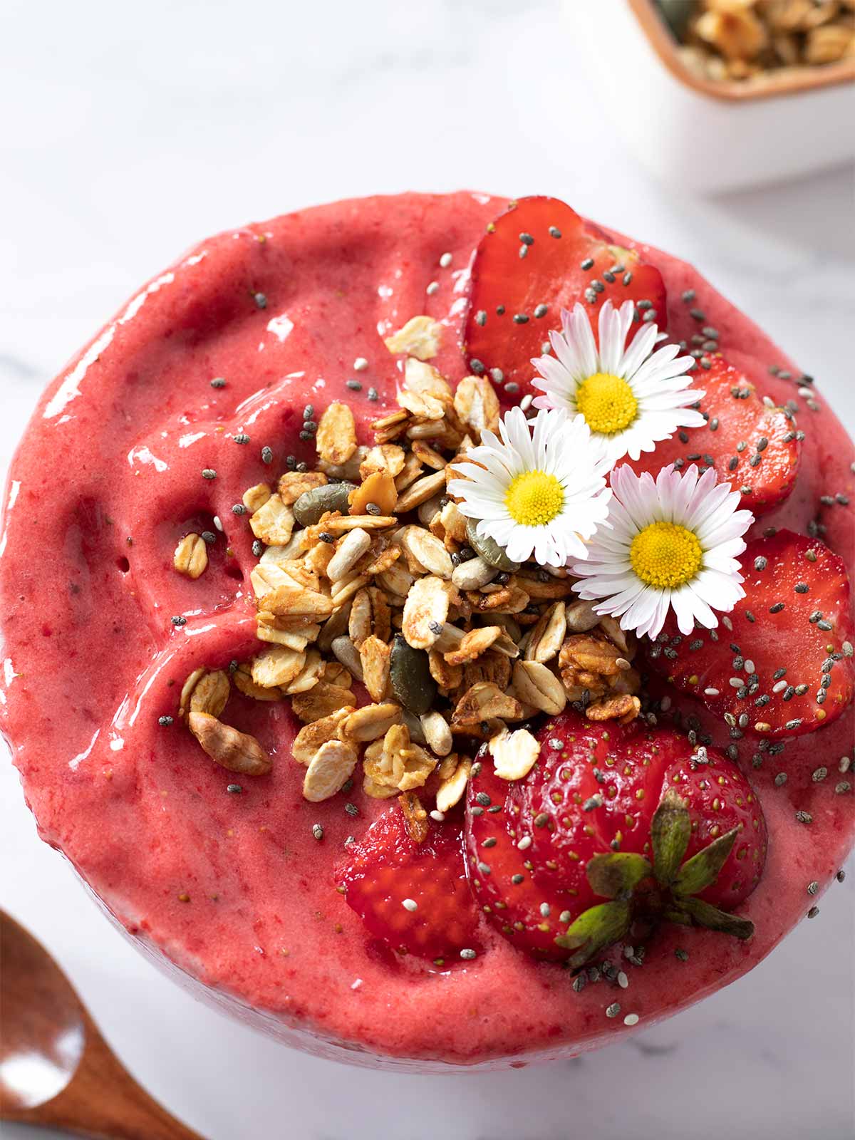 Thick and creamy strawberry smoothie bowl without banana with healthy toppings like crunchy granola and fresh strawberries