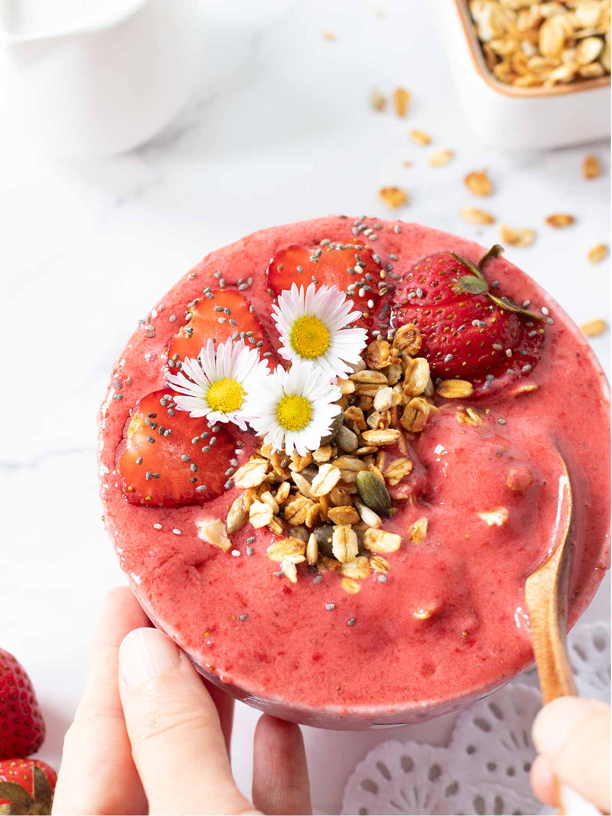 Super thick and cold no banana strawberry smoothie bowl topped with fresh strawberries, healthy homemade granola and flowers as an easy vegan summer dessert or breakfast