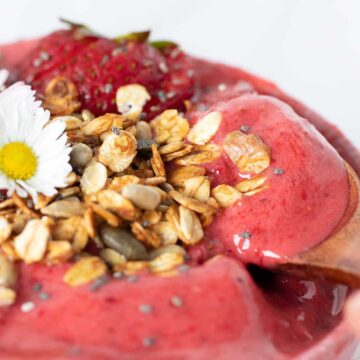 Super thick strawberry smoothie bowl without banana and healthy toppings like healthy granola and fresh fruit with wooden spoon