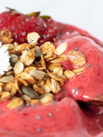 Super thick strawberry smoothie bowl without banana and healthy toppings like healthy granola and fresh fruit with wooden spoon