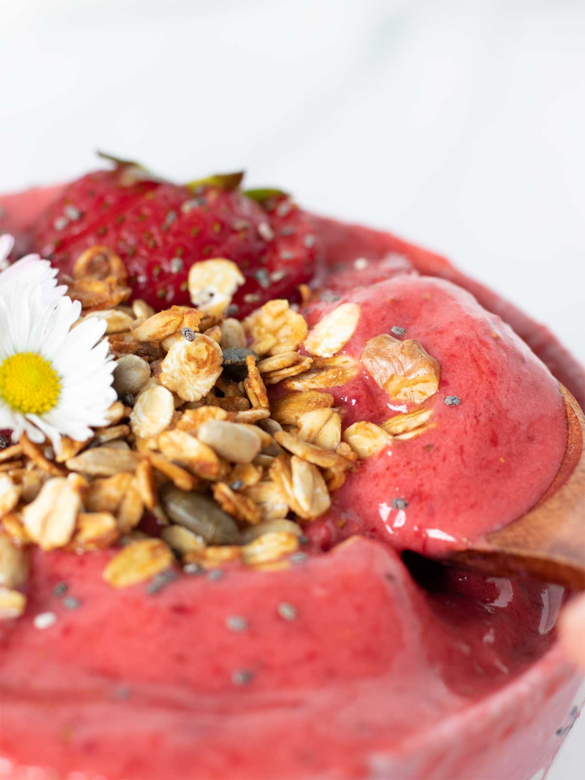 Super thick strawberry smoothie bowl without banana and healthy toppings like healthy granola and fresh fruit with wooden spoon