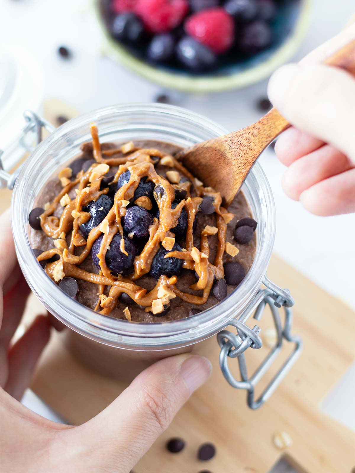 Chocolate blended overnight oats drizzled with peanut butter and frozen blueberries in a jar