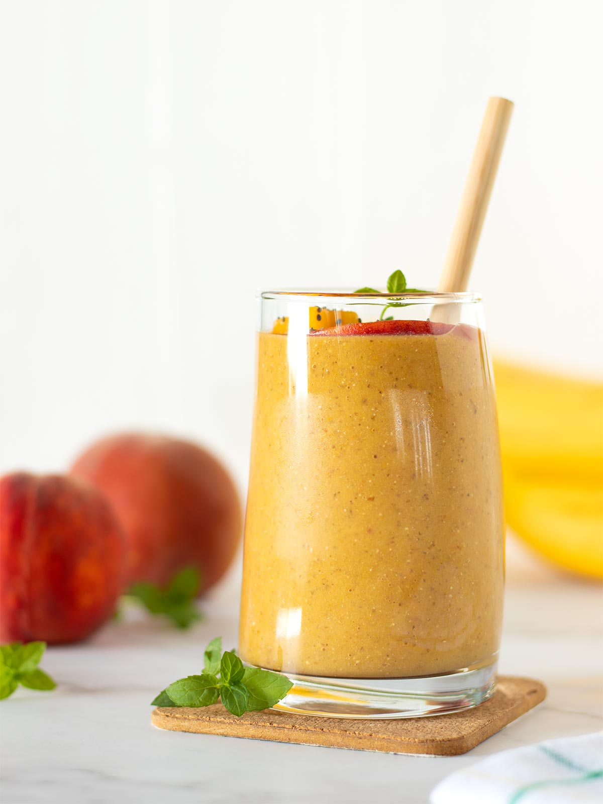 Banana peach almond milk smoothie with chia seeds and turmeric powder in a glass with bamboo straw.