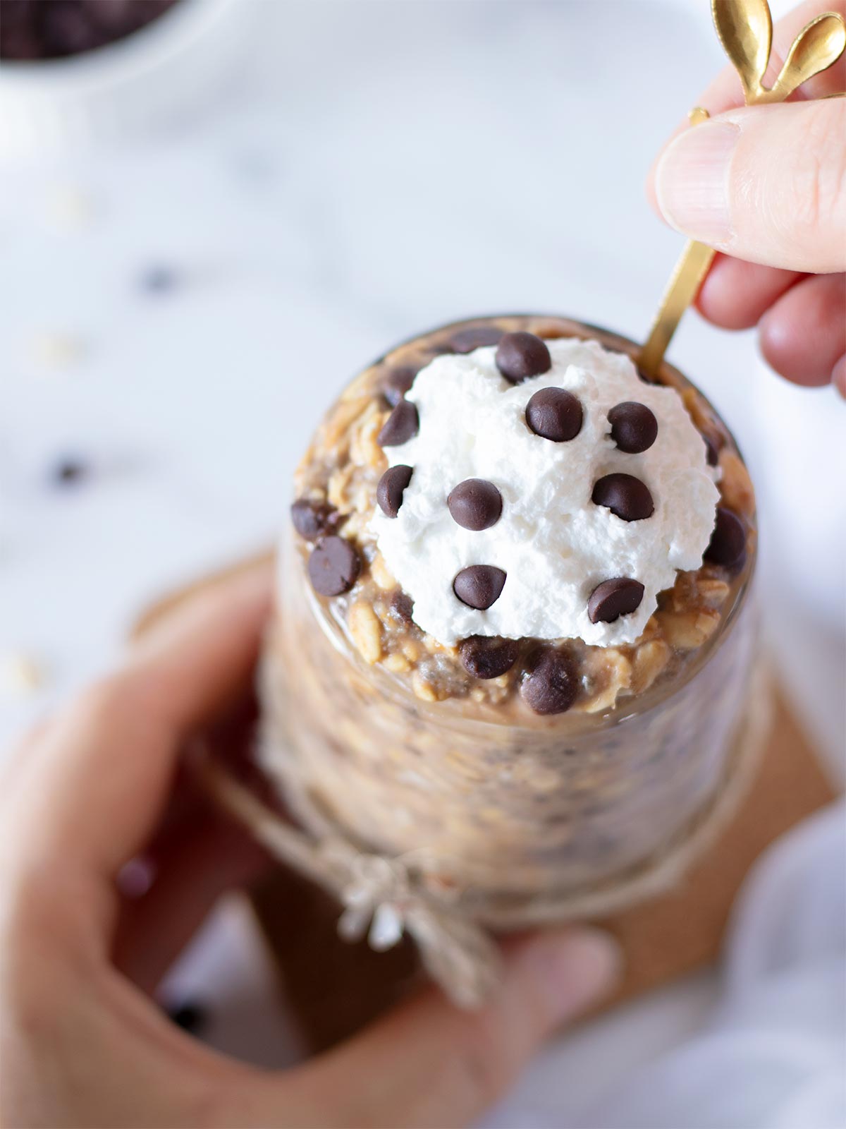 Female hands holding spoon dipped in cold vegan protein chocolate chip oatmeal with cookie dough flavor.