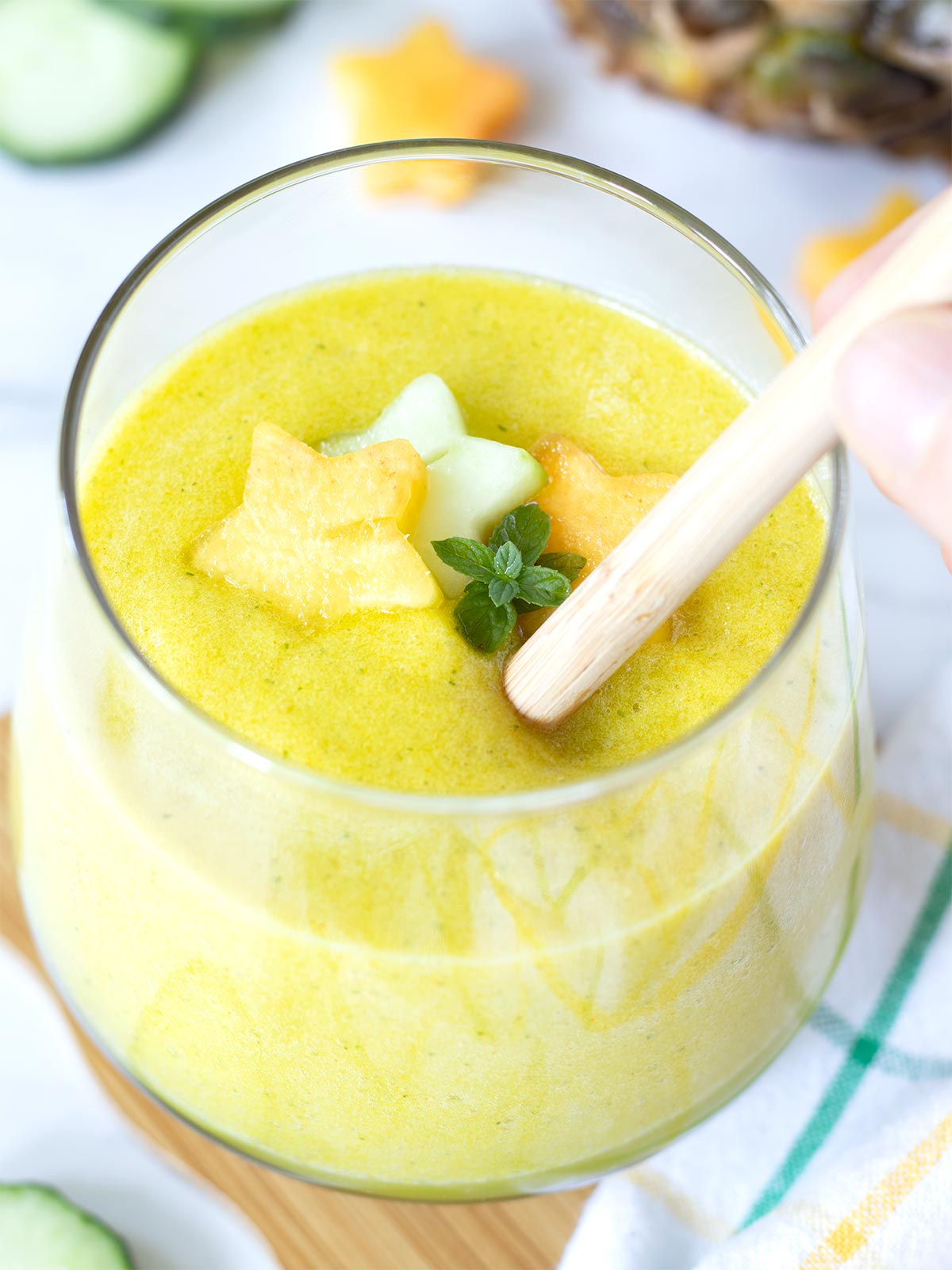 Detox pineapple cucumber lemon smoothie with bright yellow color in a glass with bamboo straw.
