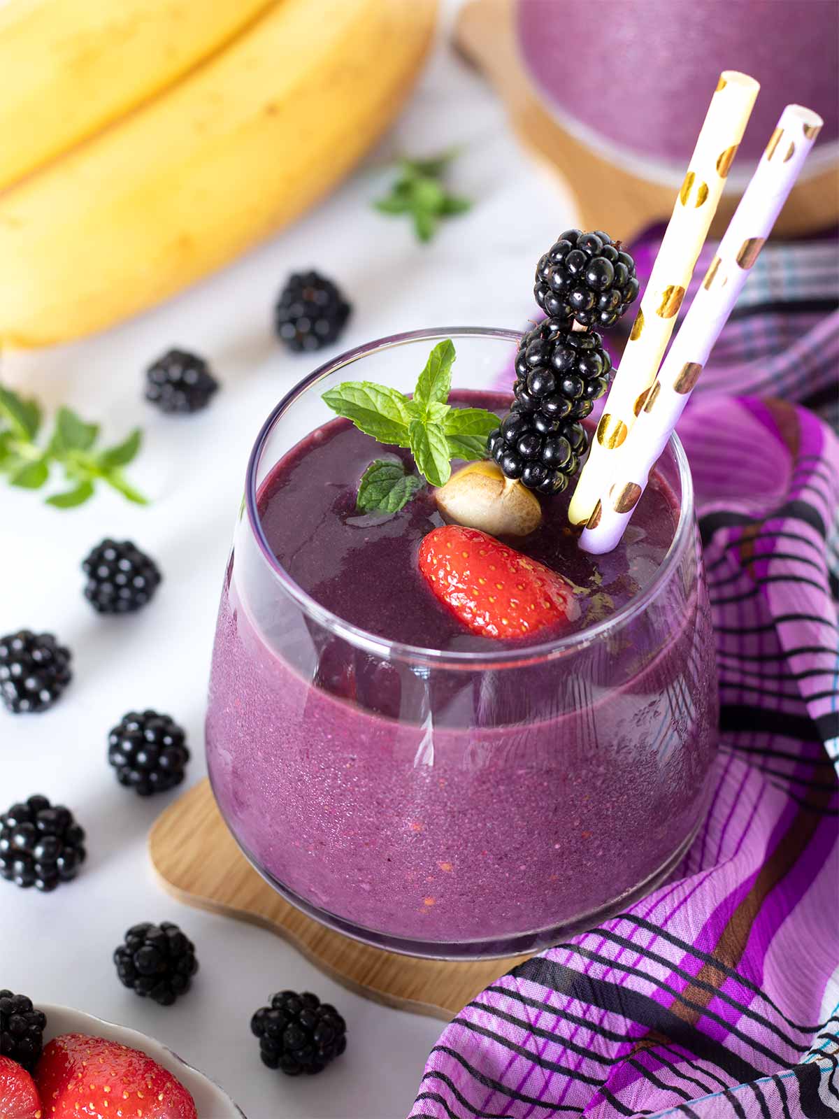 Blackberry strawberry banana smoothie without yogurt decorated with fresh mint and colorful straws.