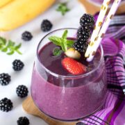 Blackberry strawberry banana smoothie without yogurt decorated with fresh mint and colorful straws.