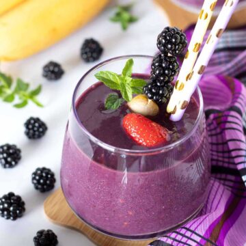 Blackberry strawberry banana smoothie without yogurt decorated with fresh mint and colorful straws.