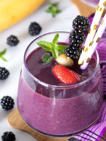 Blackberry strawberry banana smoothie without yogurt decorated with fresh mint and colorful straws.