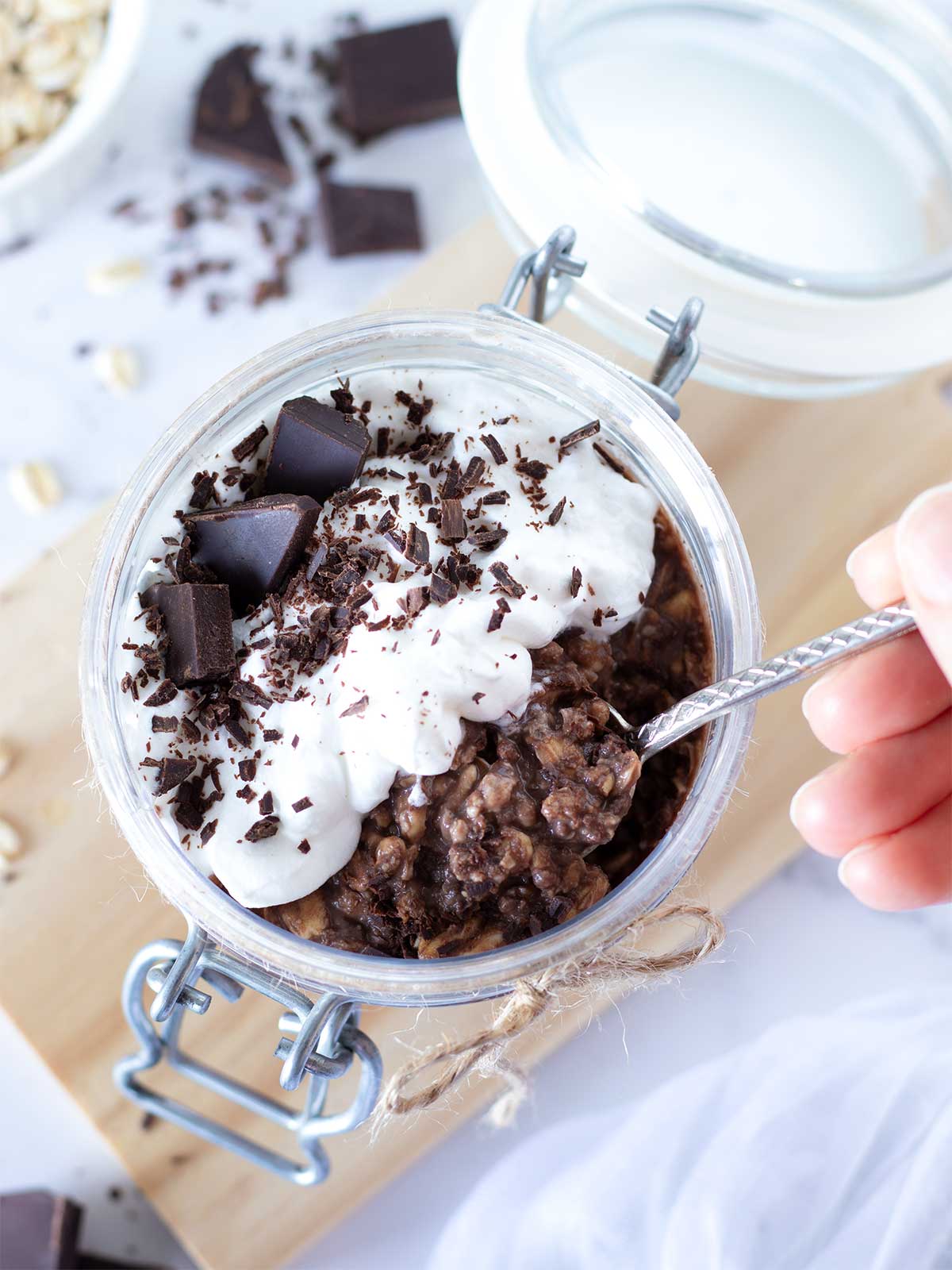 Chocolate protein overnight oats (proats) without yogurt in jar topped with whipped cream and chopped dark chocolate.