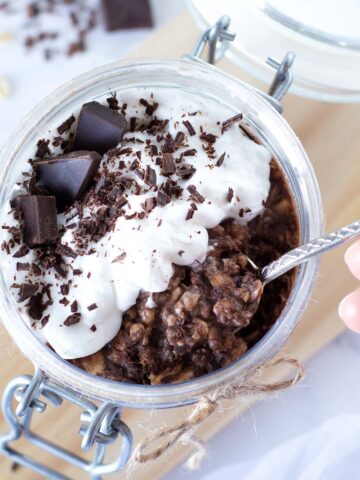 Chocolate protein overnight oats (proats) without yogurt in jar topped with whipped cream and chopped dark chocolate.