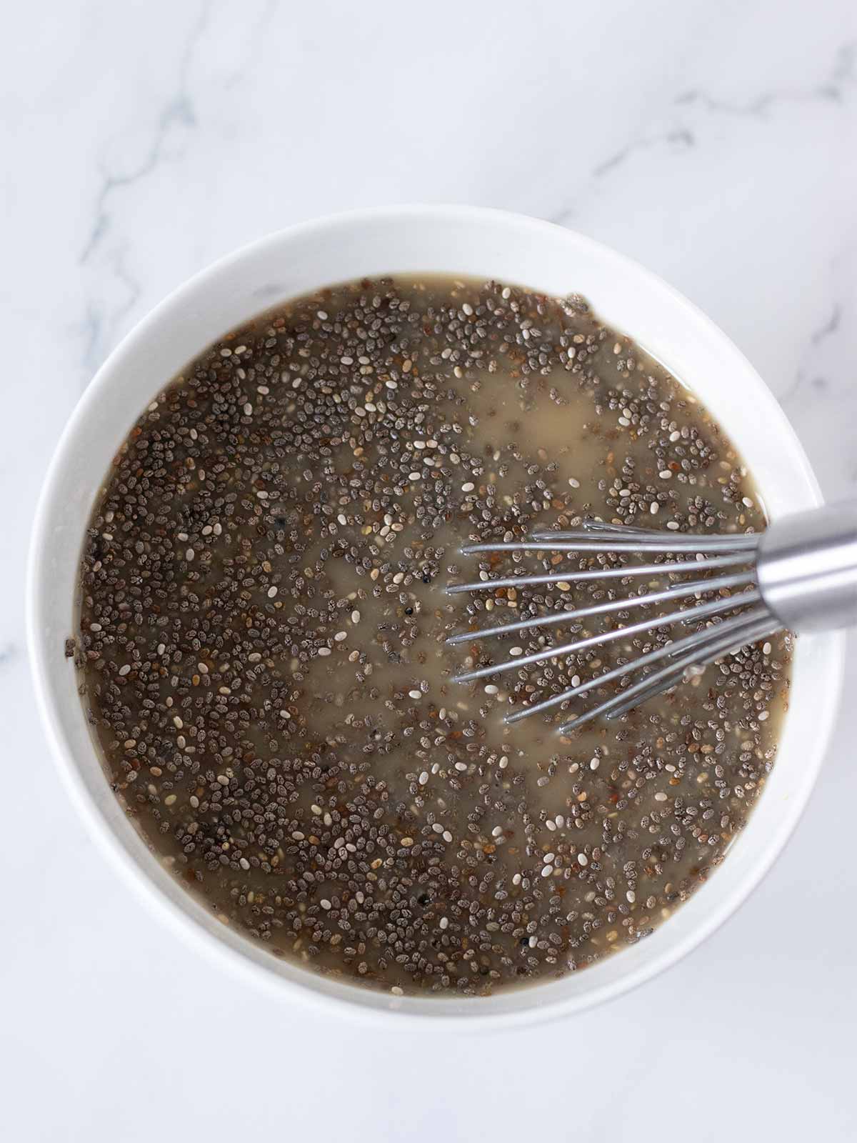 Preparing a healthy chia seed pudding in a bowl with a whisk.