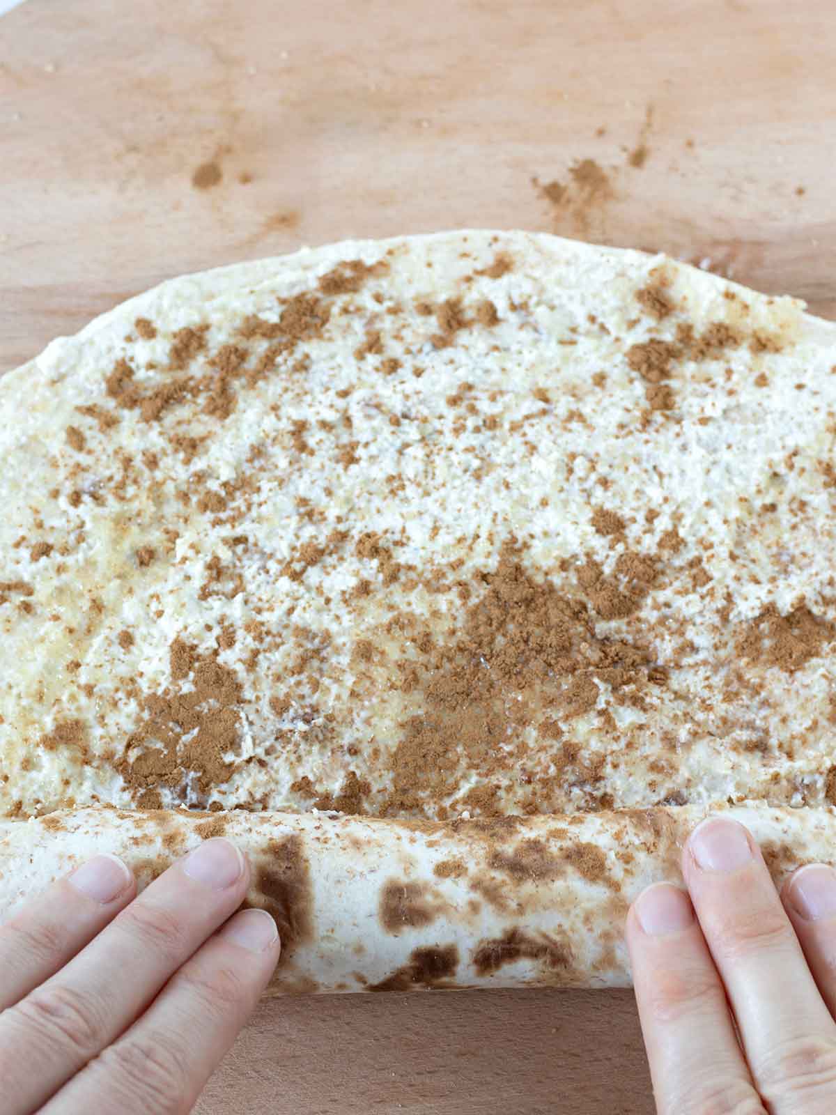 Hands rolling sweet cinnamon sugar tortillas with cream cheese.