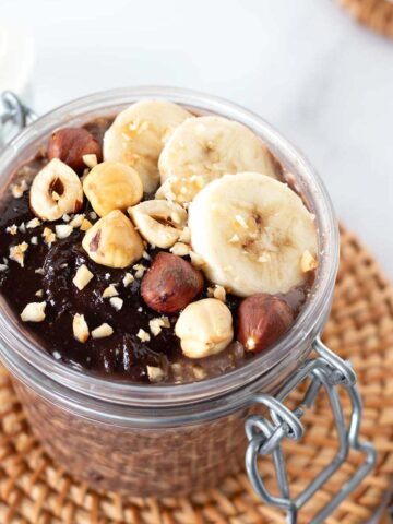 Nutella overnight oats in a jar topped with hazelnuts and sliced bananas.