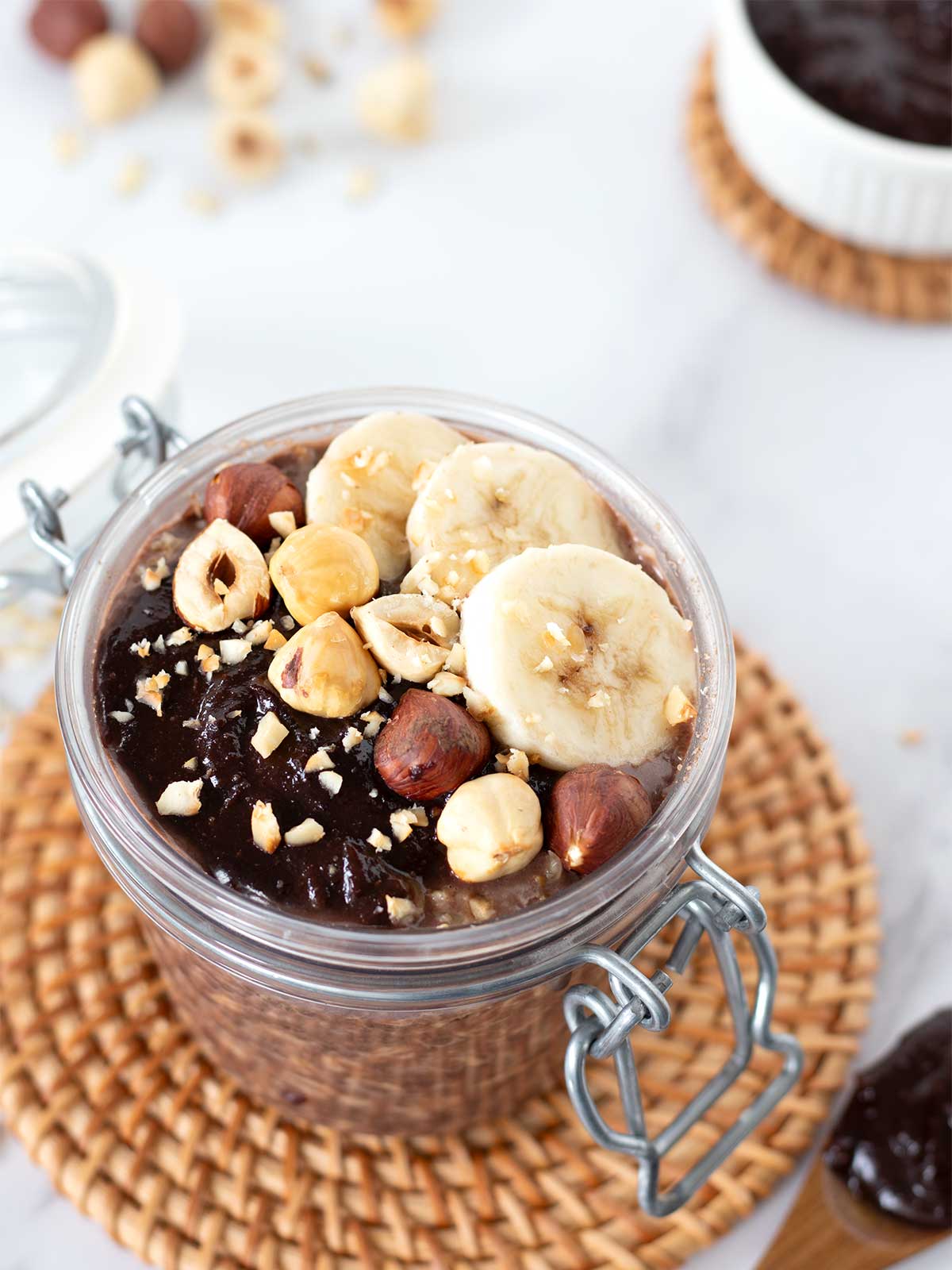 Nutella overnight oats in a jar topped with hazelnuts and sliced bananas.