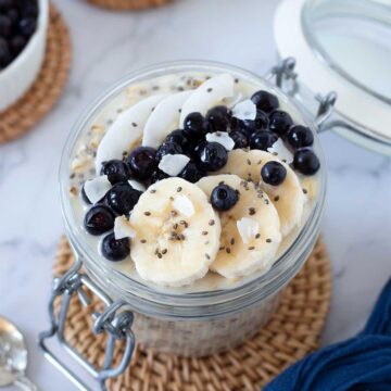 Overnight oats with water topped with chia seeds, banana slices, blueberries, and coconut flakes.