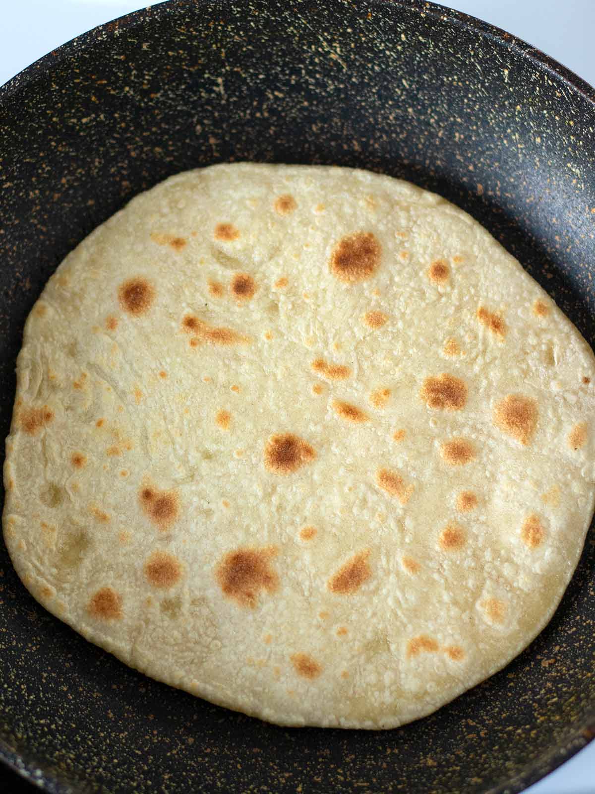 Bread without yeast is cooking in frying pan on the stovetop.